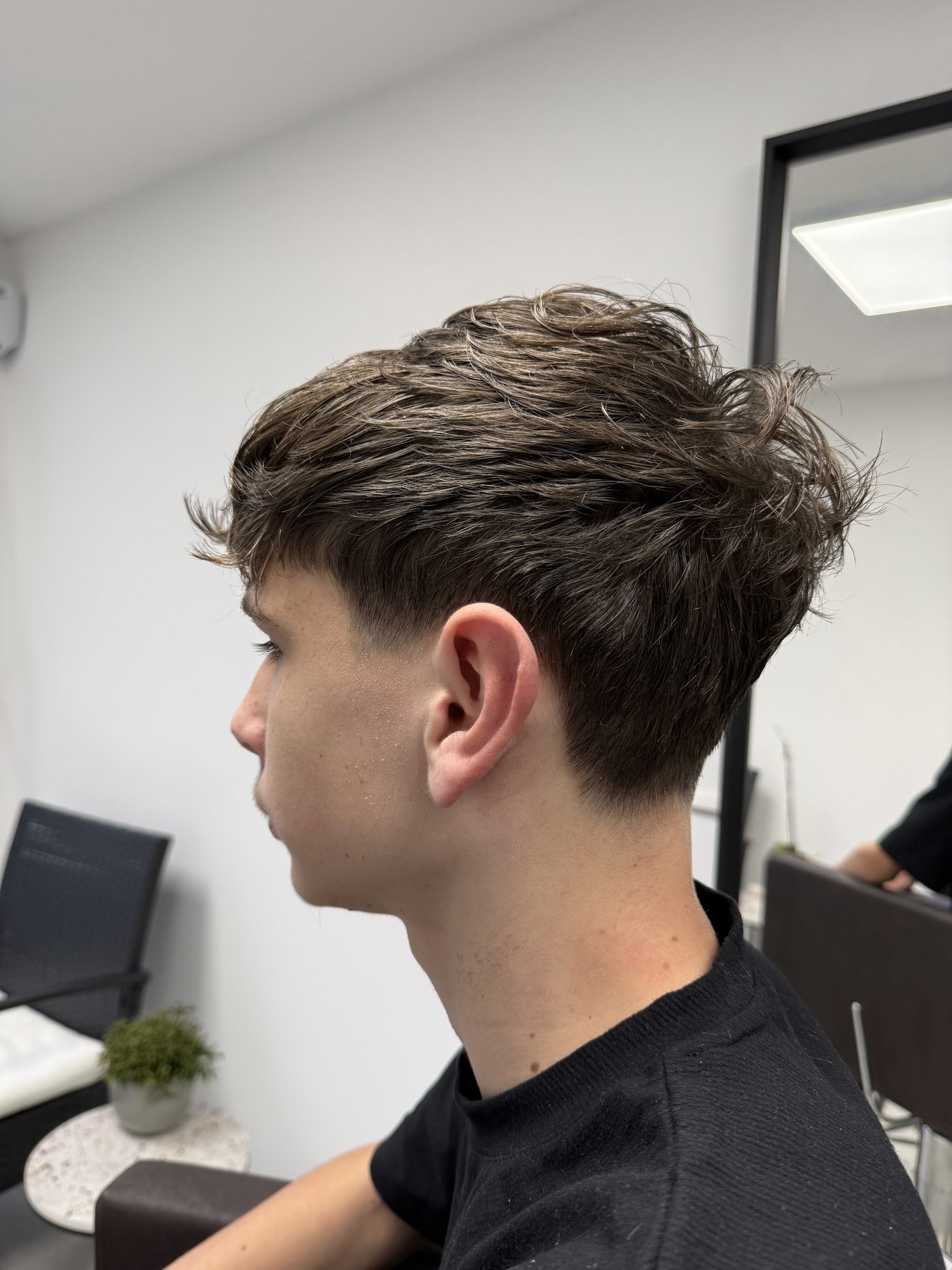 Jonge klant van opzij met een textured crop en een fade in de nek, net geknipt